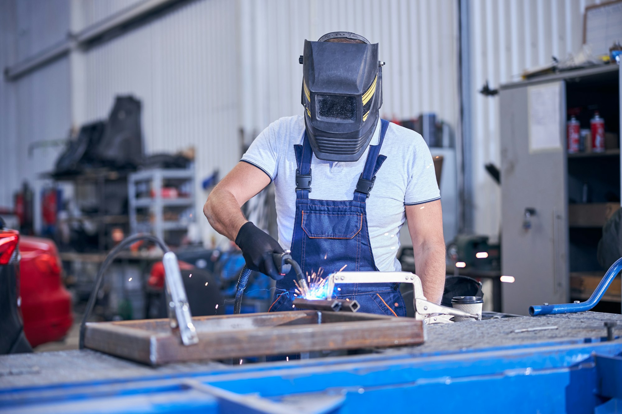 Male worker in welding helmet welding metal in garage